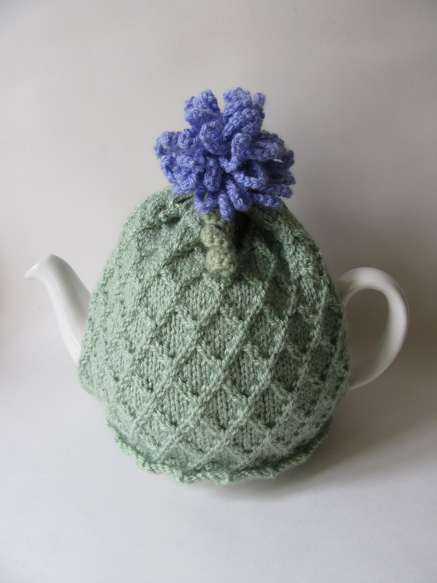 Knitted pastel green trellis tea cosie with allium flower