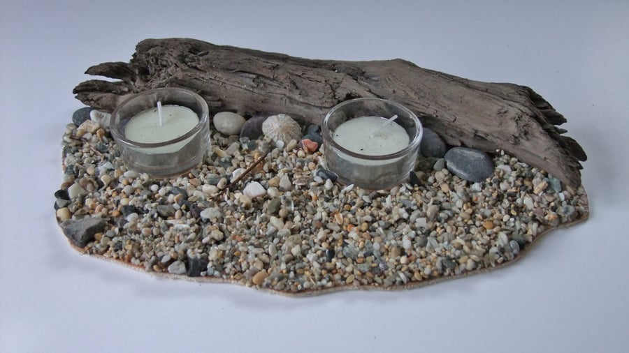 Twin glass tealight holder & tealight on pebble beach with a driftwood backdrop.