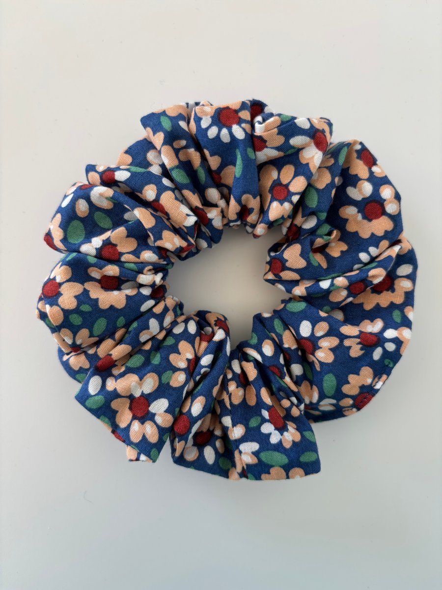 Cotton scrunchie hair accessory in a daisy floral print on blue background