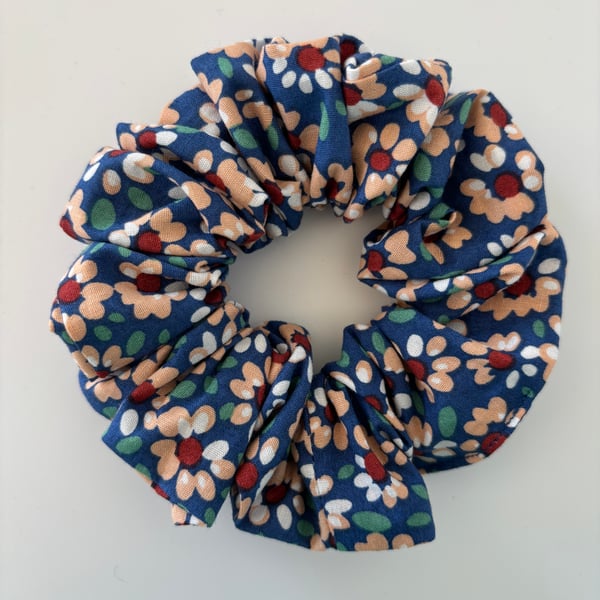 Cotton scrunchie hair accessory in a daisy floral print on blue background