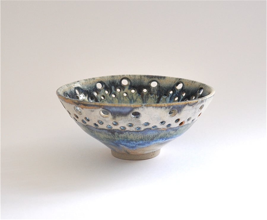 Decorative ceramic bowl with perforated rim in shades of cream, green and blue