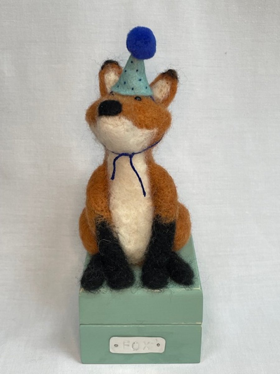 Handcrafted needle felted fox with removable party hat on a wooden box