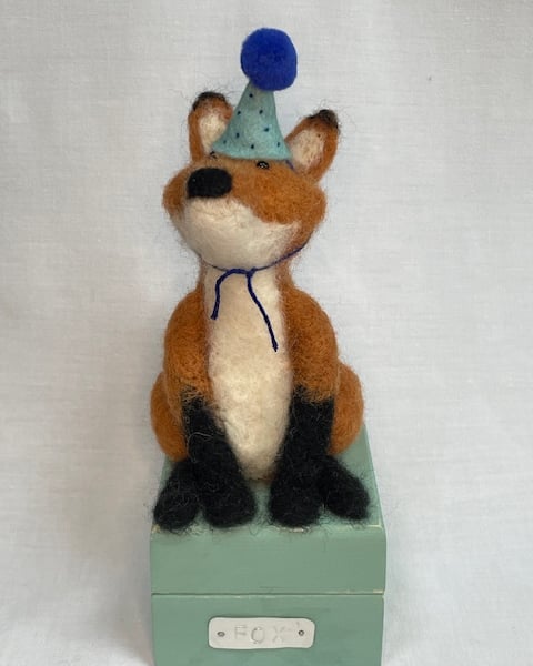 Handcrafted needle felted fox with removable party hat on a wooden box