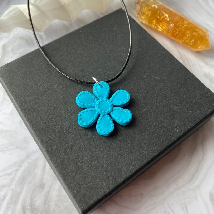 Flower statement pendant in turquoise blue polymer clay on a black cord chain.