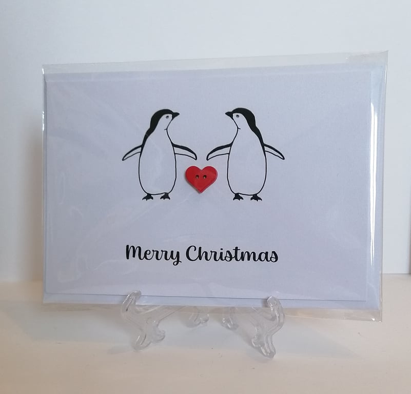 Merry Christmas card with two penguins and a red heart button