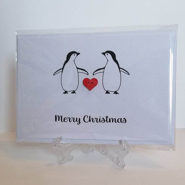 Merry Christmas card with two penguins and a red heart button