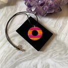 Pink and orange striped donut circle pendant on a black cord necklace.