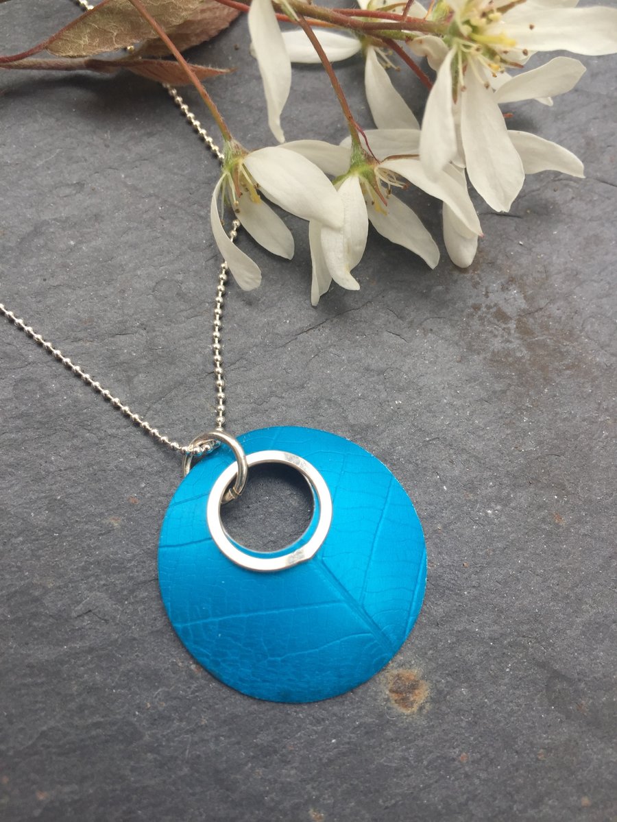 Turquoise, circular, leaf textured, anodised aluminium pendant with silver ring