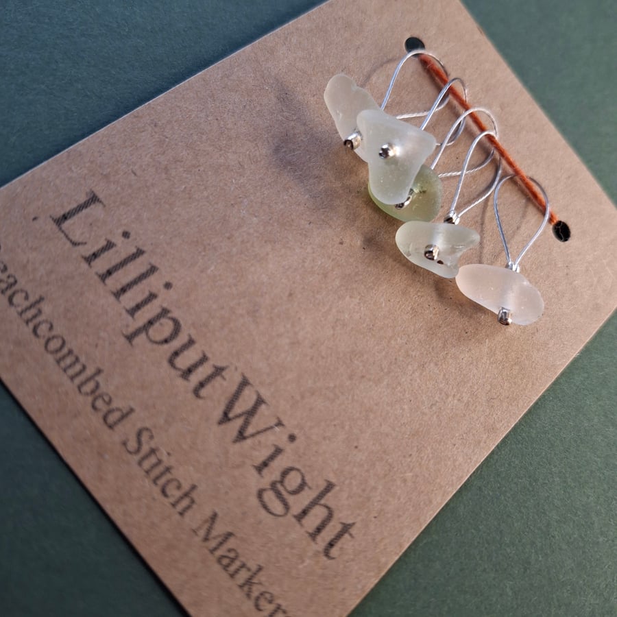 Five sea glass stitch markers in shades of white and pale green