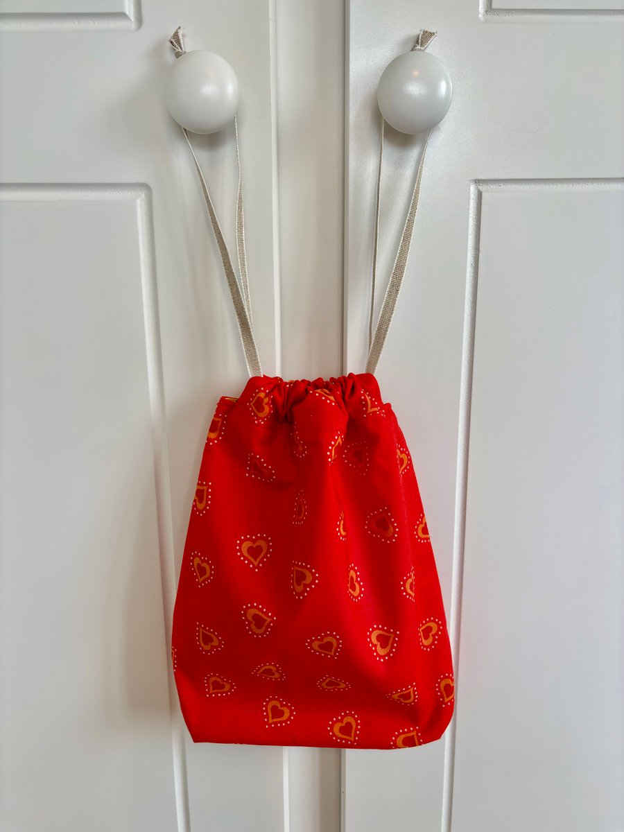 Red cotton drawstring bag with red and orange hearts, with linen style ribbon.