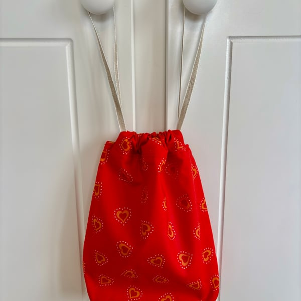 Red cotton drawstring bag with red and orange hearts, with linen style ribbon.