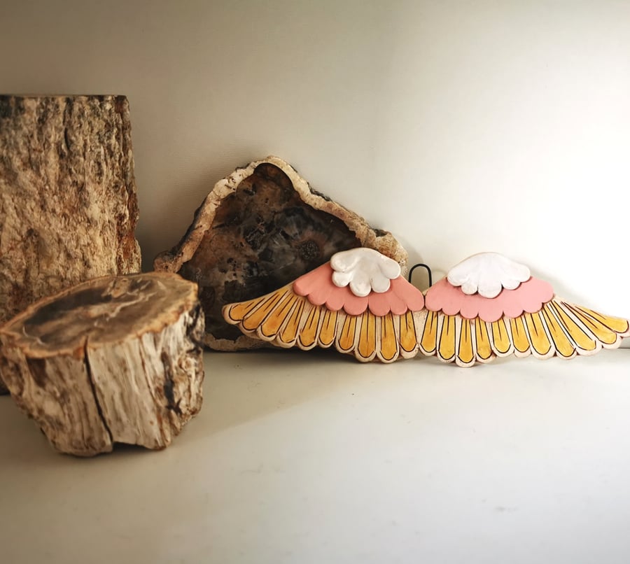 Glazed ceramic winged decoration in pink, white and yellow ochre 