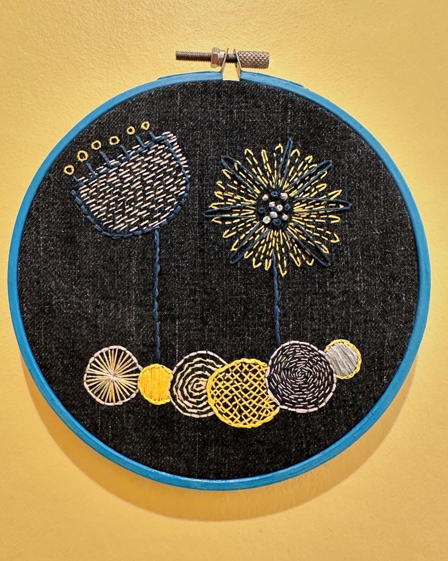 Denim wall hanging with embroidered abstract flower art in blue hoop frame. 