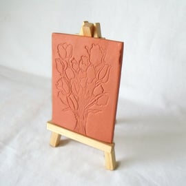 terracotta impressed clay tile displayed on an easel, floral design 