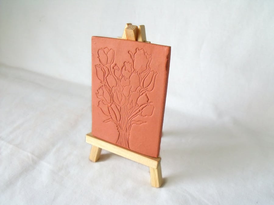 terracotta impressed clay tile displayed on an easel, floral design 