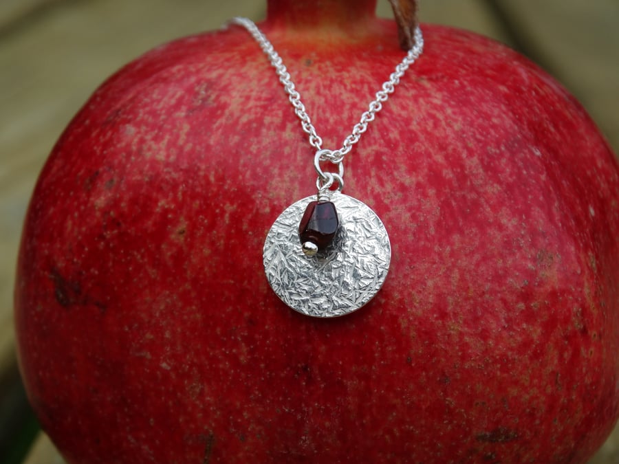 Winter's Return textured recycled silver disc pendant, garnet pomegranate seed