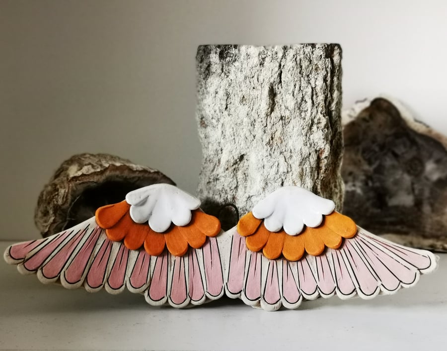 Glazed ceramic winged decoration in tawny orange, white and pink