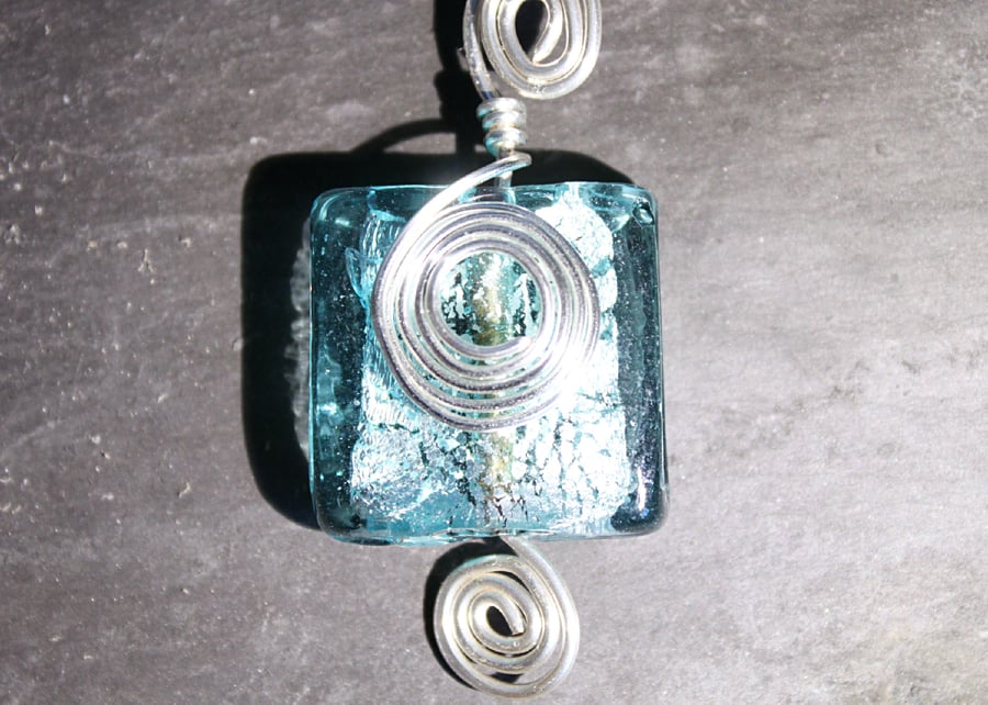 Square light blue foiled glass bead wrapped in spirals of silver wire pendant