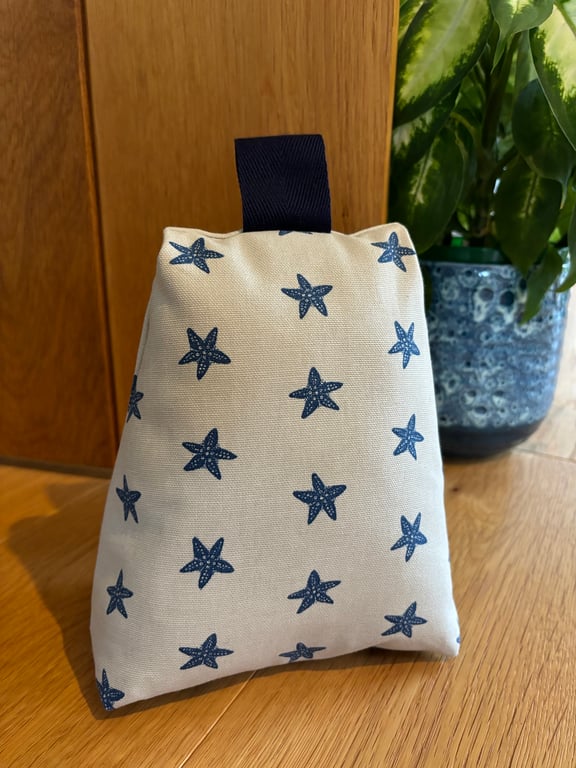 Cotton fabric doorstop in taupe with navy starfish print, filled with pebbles.