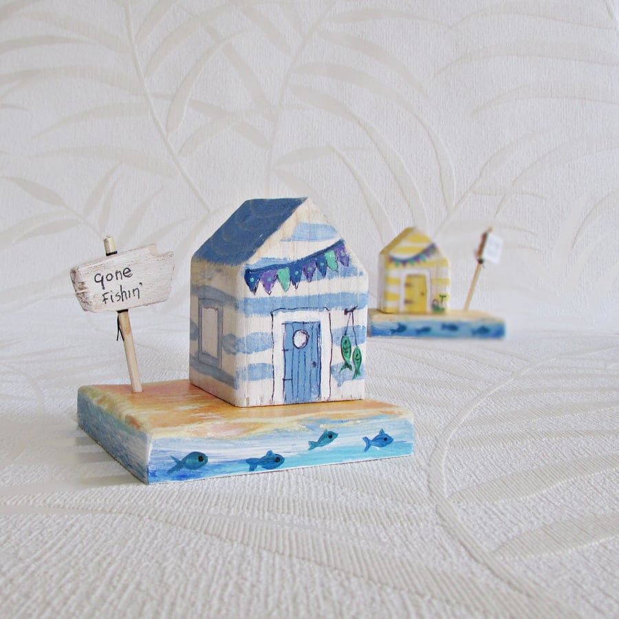 A Little Wooden Beach Hut House, on a base and a wooden sign.