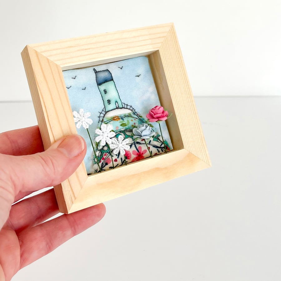 Little house on a fabric hill, with flowers, in small wooden frame