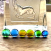 A card of six curious mixed fused glass cabochons , in blues and greens. 