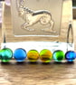 A card of six curious mixed fused glass cabochons , in blues and greens. 