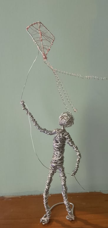Figure sculptured out of wire flying a kite 