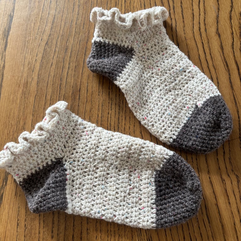 A pair of handmade cream and grey crochet socks with a frilly top in UK size 4