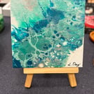 Easel mounted acrylic painted canvas in greens and blues