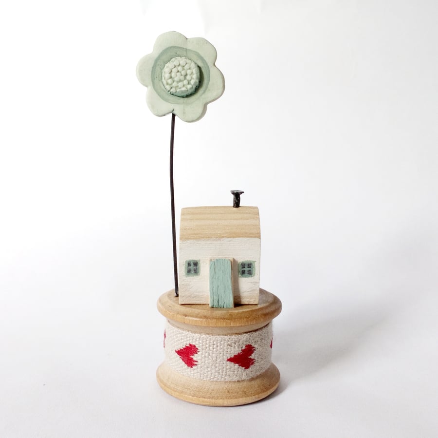 Tiny oak house with clay flower on vintage wooden bobbin