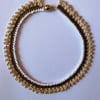 A crocheted necklace in white, coffee and cream cotton with edging of gold beads