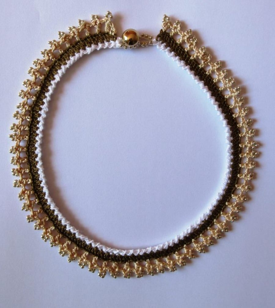 A crocheted necklace in white, coffee and cream cotton with edging of gold beads