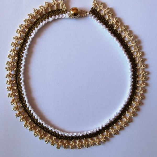 A crocheted necklace in white, coffee and cream cotton with edging of gold beads