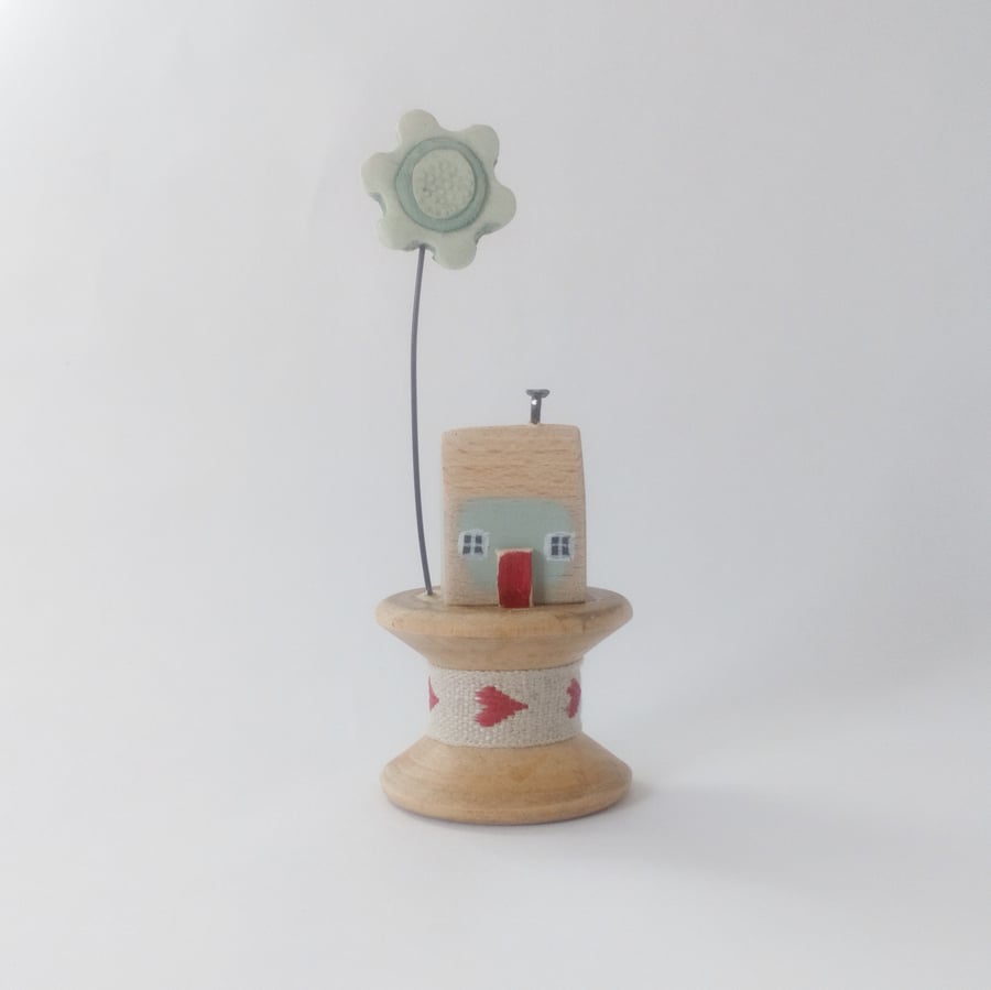 Tiny oak house with clay flower on vintage wooden bobbin