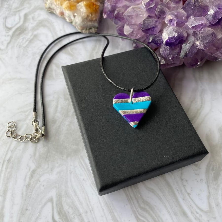 Blue and purple striped heart pendant on a black cord necklace.