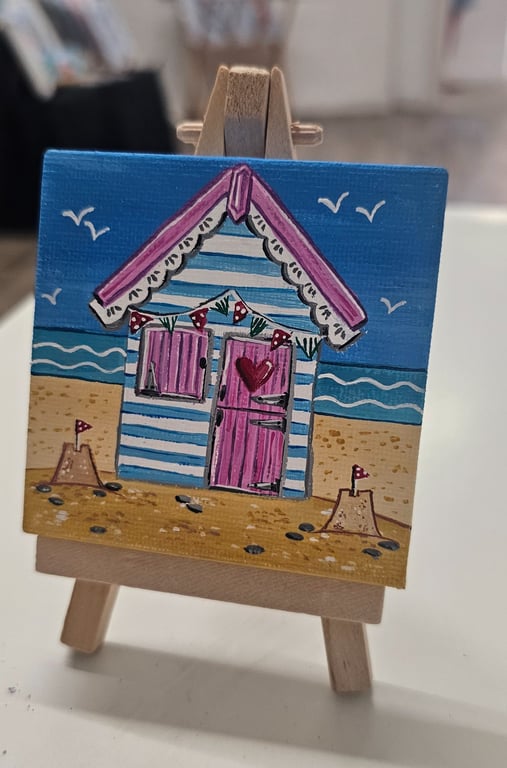 Cute little canvas of a pink and blue beach hut on a little easel.