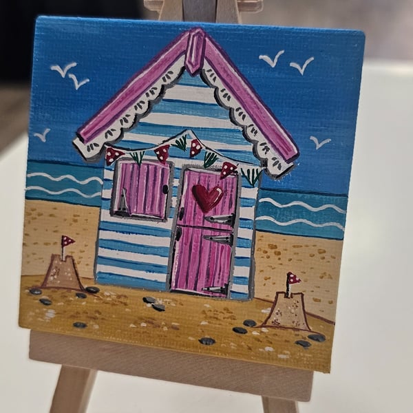 Cute little canvas of a pink and blue beach hut on a little easel.