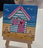 Cute little canvas of a pink and blue beach hut on a little easel.