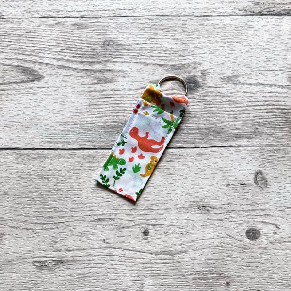 Dinosaur lip balm white polycotton fabric keyring.