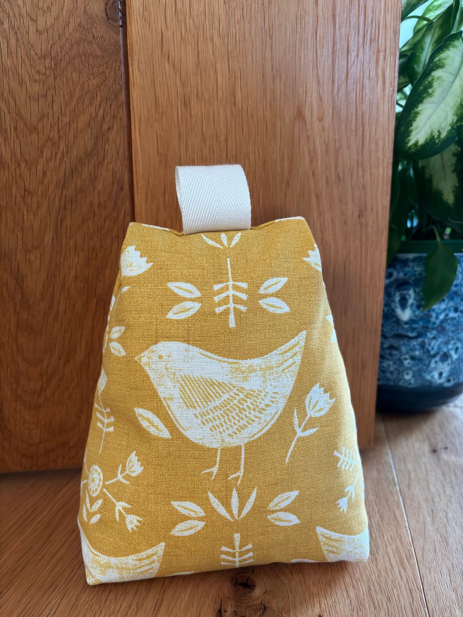 Cotton fabric doorstop in ochre with white bird print, filled with pebbles.