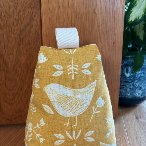 Cotton fabric doorstop in ochre with white bird print, filled with pebbles.