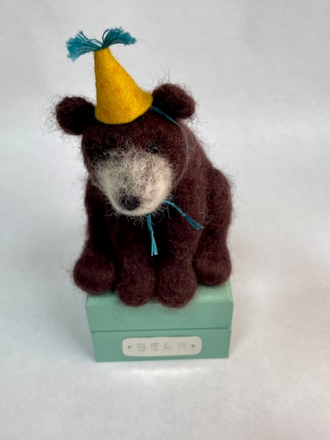 Handcrafted needle felted brown bear with removable party hat on a wooden box