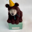 Handcrafted needle felted brown bear with removable party hat on a wooden box
