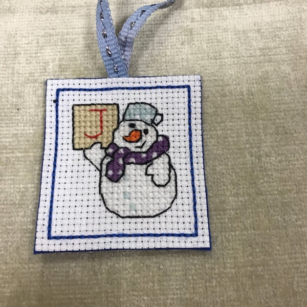 Cross stitched snowman holding a letter J. Cute Christmas tree decoration snowma