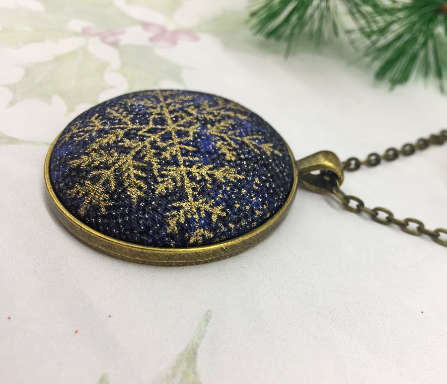Gold metallic snowflake fabric button pendant on a deep blue background