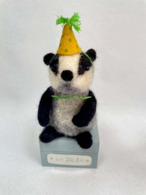 Handcrafted needle felted badger with removable party hat on a wooden box