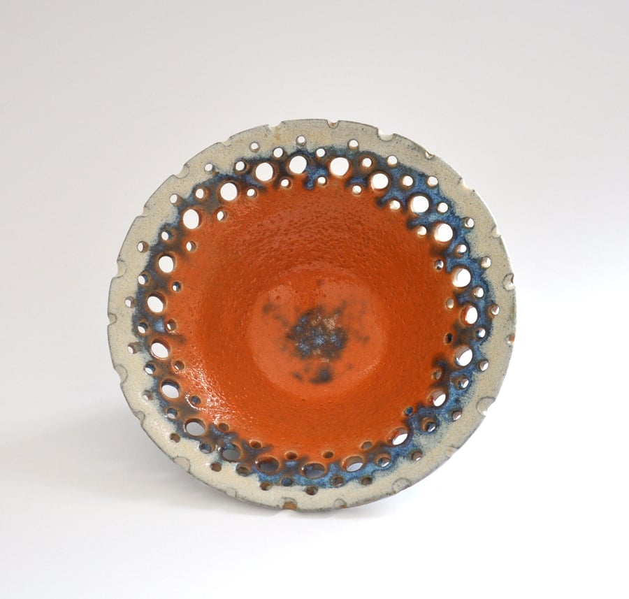 Decorative ceramic bowl with perforated rim in shades of orange, blue and chalk