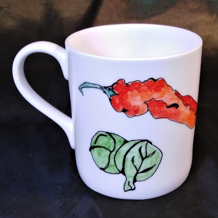 A beautiful pure white bone china mug hand decorated with vegetables. An aubergi