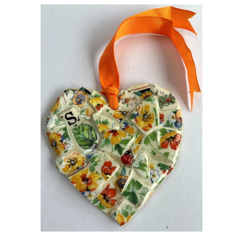 A heart shaped mosaic pendant with a wild flowers theme in orange and green.
